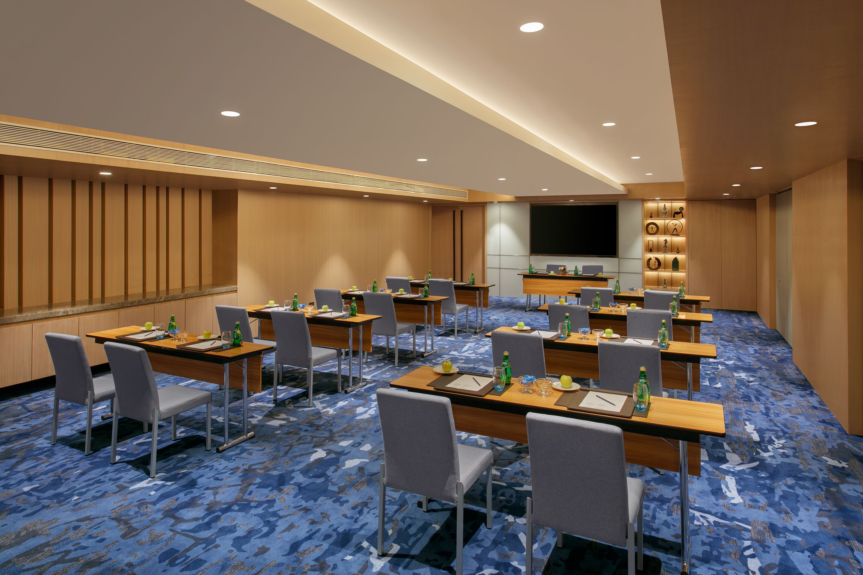 A conference room with multiple tables, chairs, and a large screen.