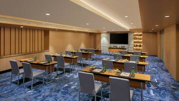 A conference room with multiple tables, chairs, and a large screen.