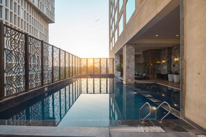 Ein innenliegender Schwimmteich mit modernem Design, umgeben von einer gemusterten Umzäunung und einem Gebäude mit großen Fenstern.