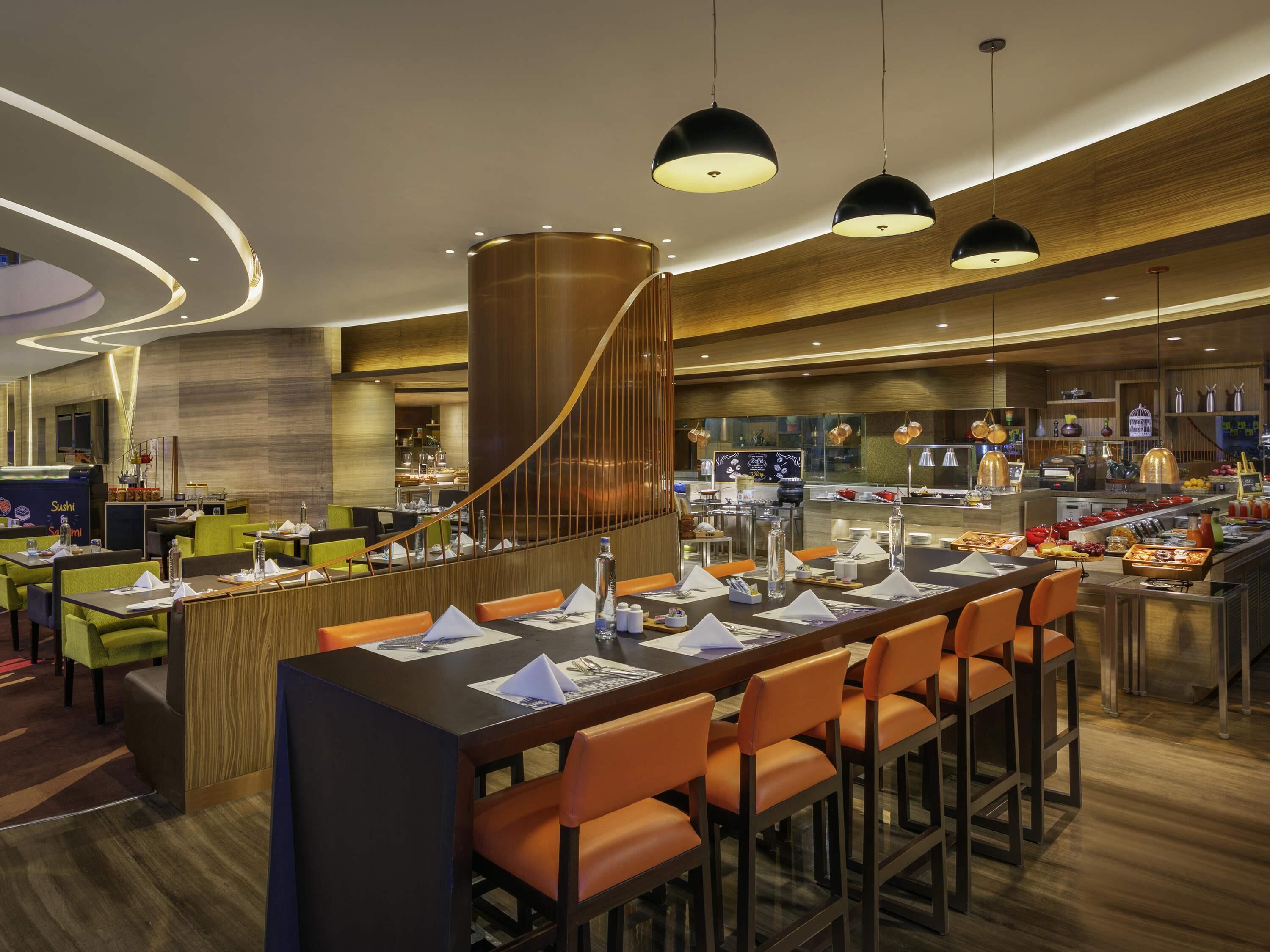 A modern restaurant with a long bar, orange chairs, and a sushi bar in the background.