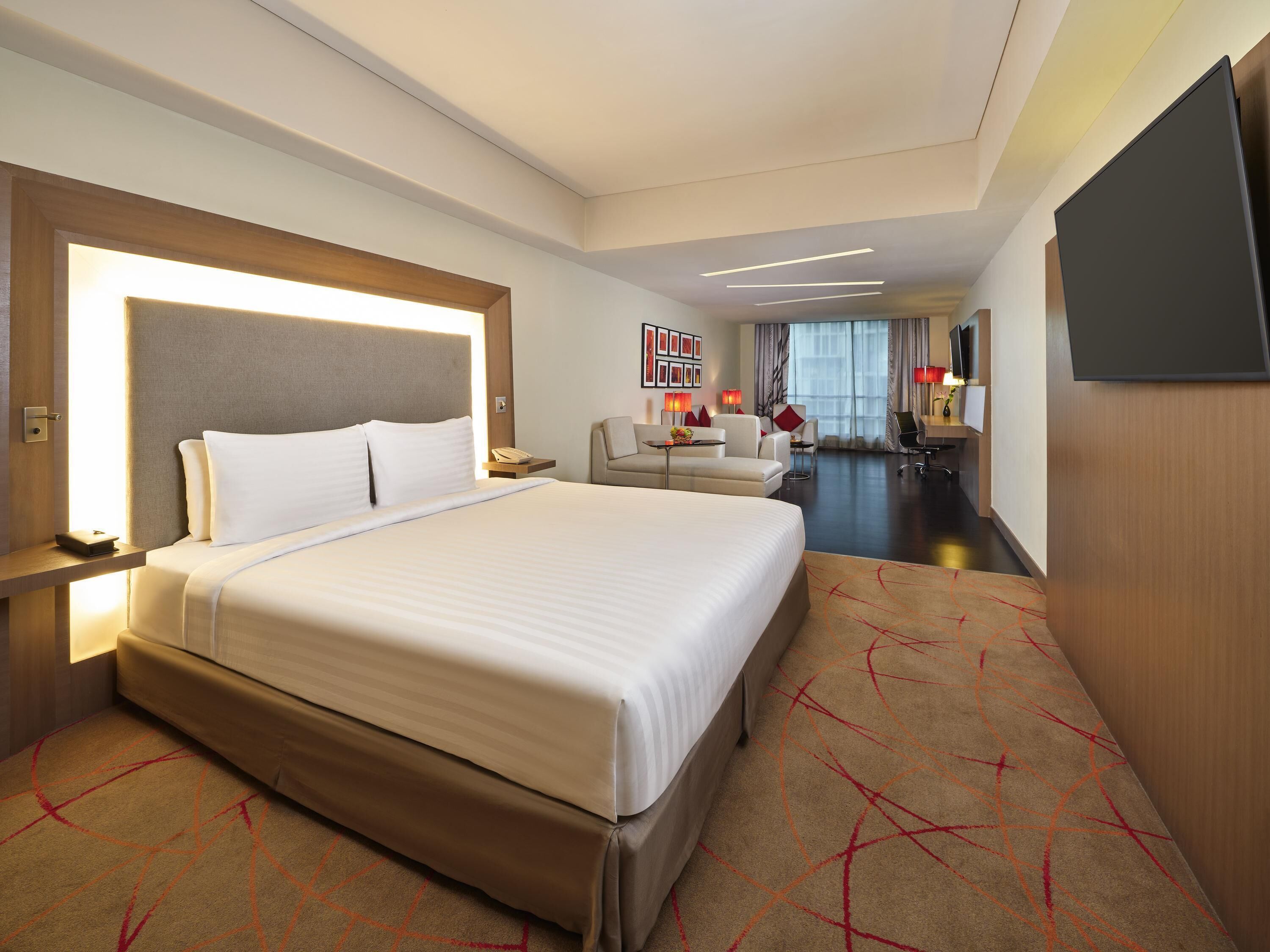 Ein Hotelzimmer mit einem großen Bett, einem Schreibtisch, einem Sessel, einer Couch, einem Fernseher und einem Fenster mit Vorhängen.