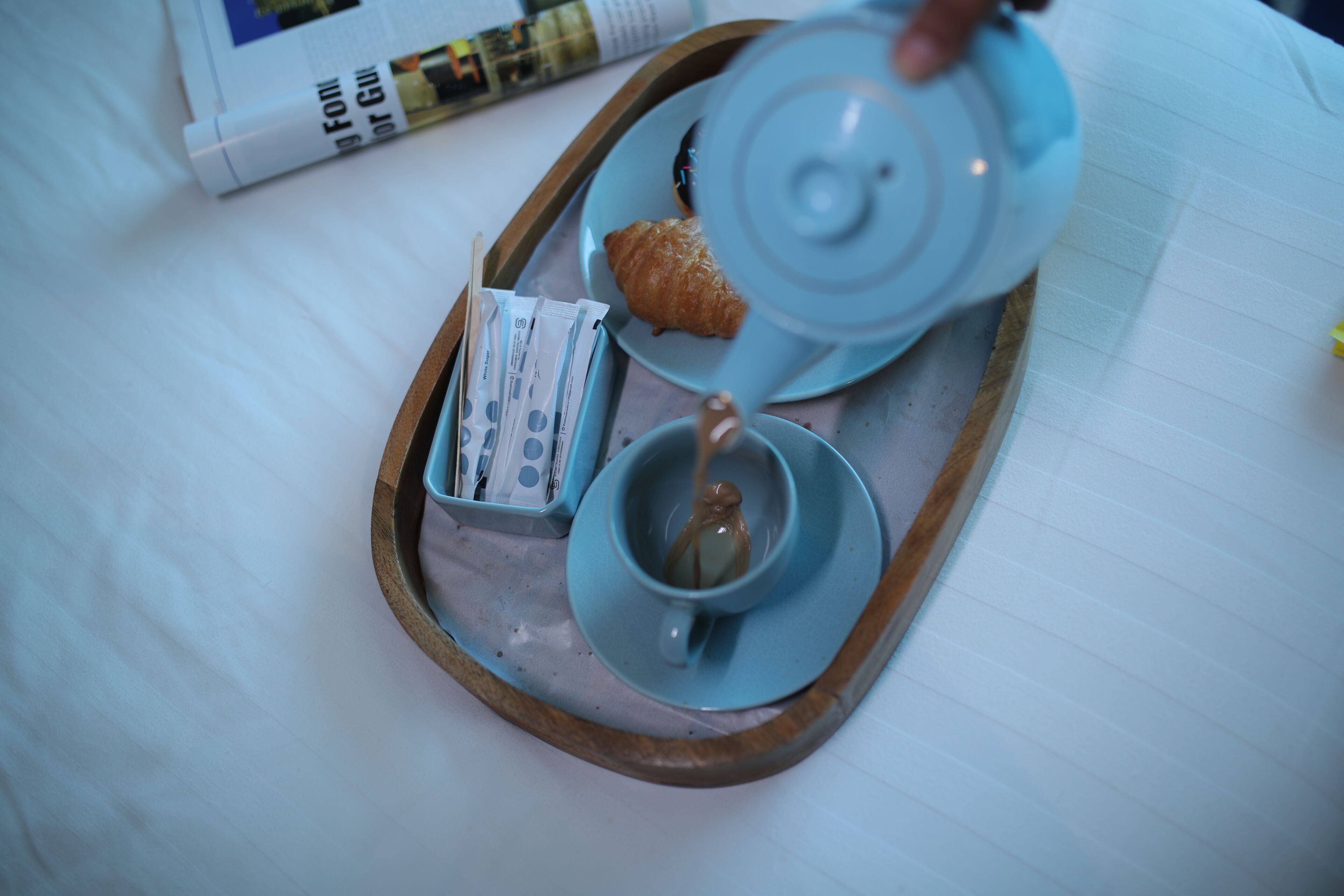 Een dienblad met een theepot, een kopje, een croissant en een zakje suikerklontjes.