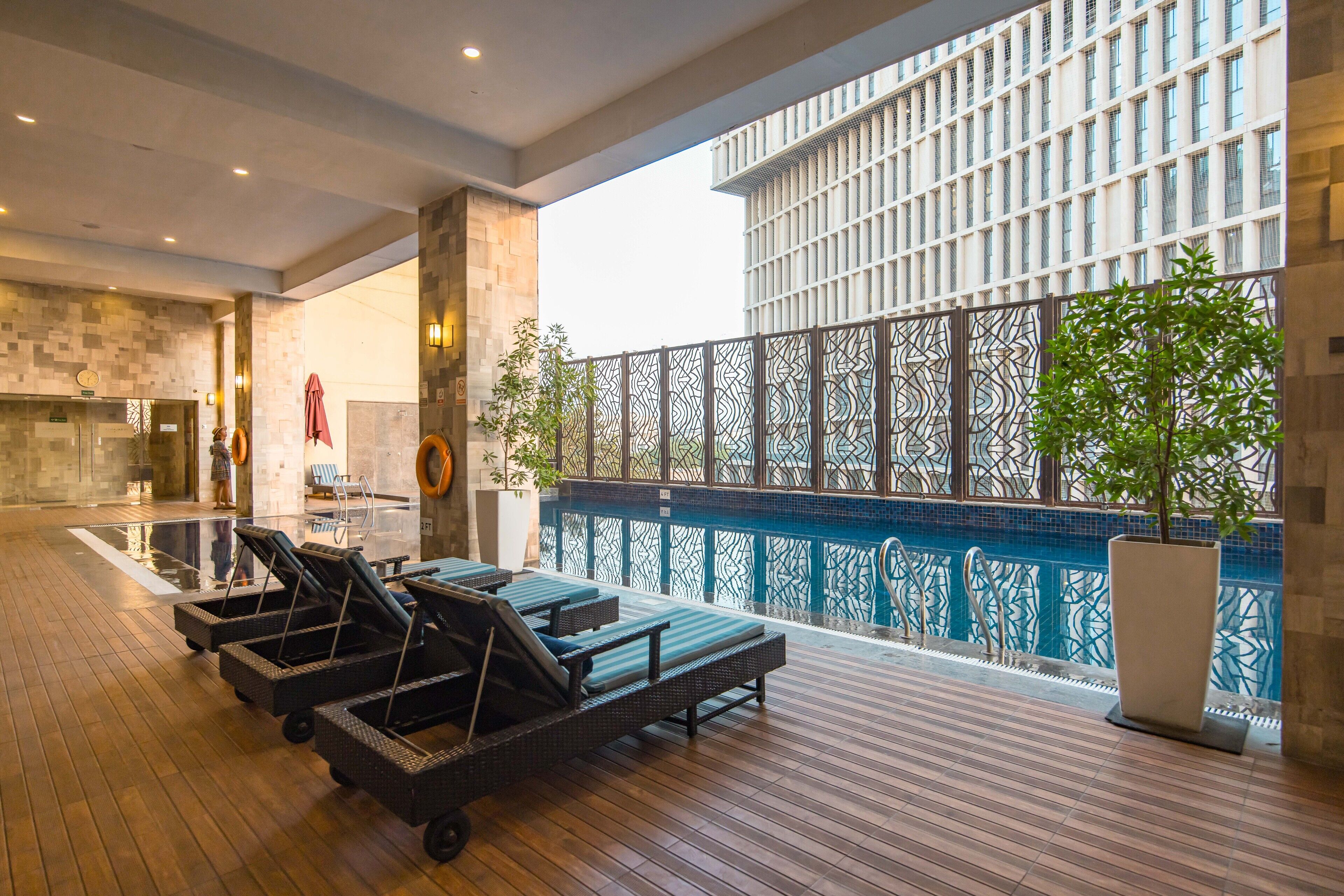 Vestíbulo de hotel con zona de piscina, sillones de descanso y un amplio ventanal con vistas a la piscina.