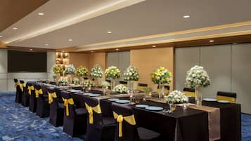 A conference room with long tables, chairs with yellow sashes, and floral centerpieces.