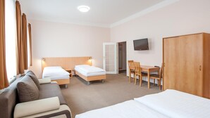 A hotel room with two single beds, a sofa, a desk with a chair, a wardrobe, and a TV on the wall. - Hotel v Centru (Ceske Budejovice)
