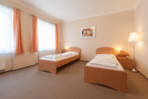 A hotel room with two single beds, a bedside table with a lamp, a small bedside table with a phone, and a framed picture on the wall. - Hotel v Centru (Ceske Budejovice)