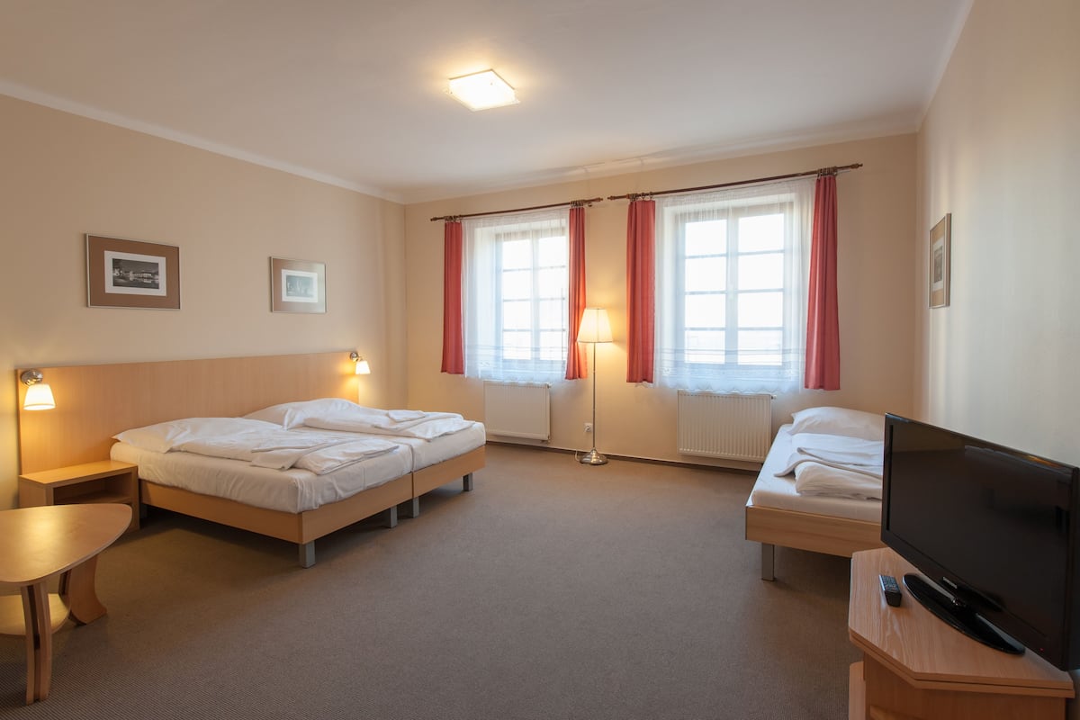 A hotel room with two beds, a TV, a lamp, and framed pictures on the wall.