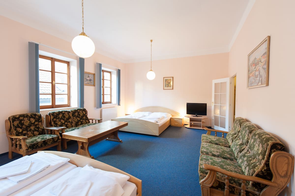 A hotel room with a bed, two armchairs, a sofa, a dining table, a TV, and a window.