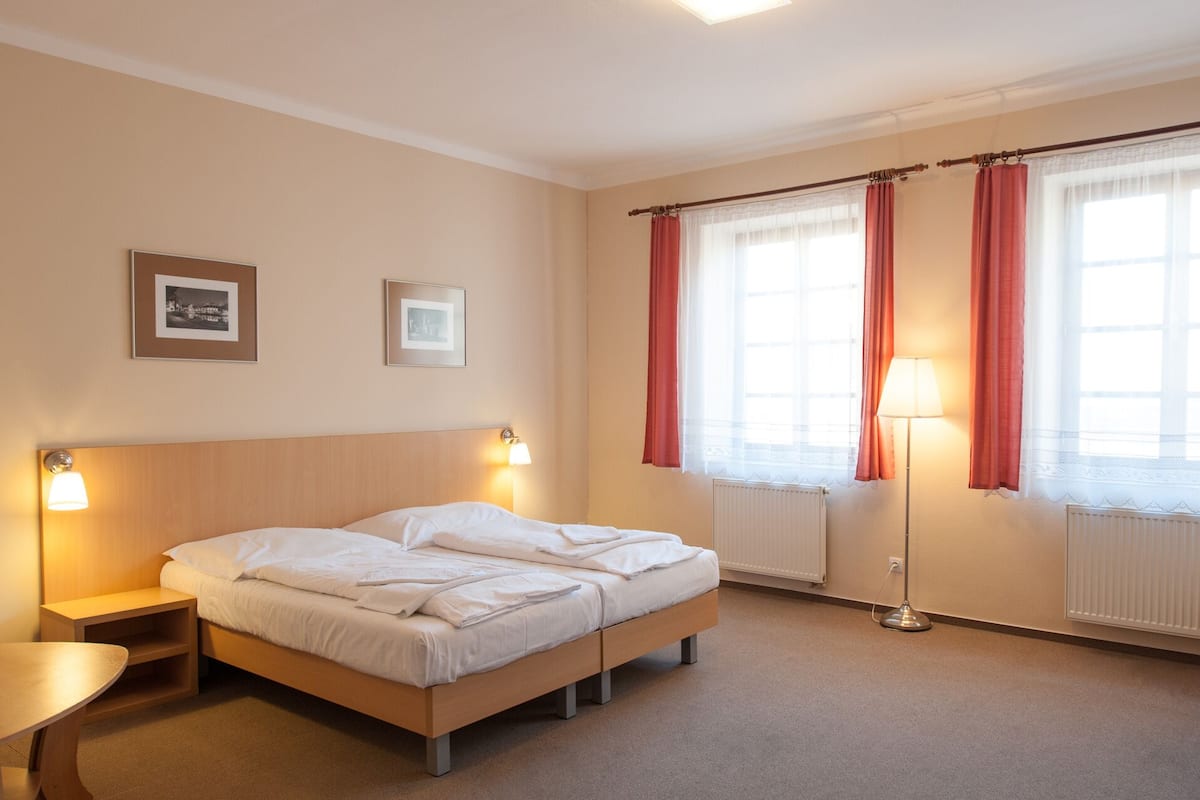 A hotel room with a double bed, two bedside tables, a floor lamp, and two framed pictures on the wall.