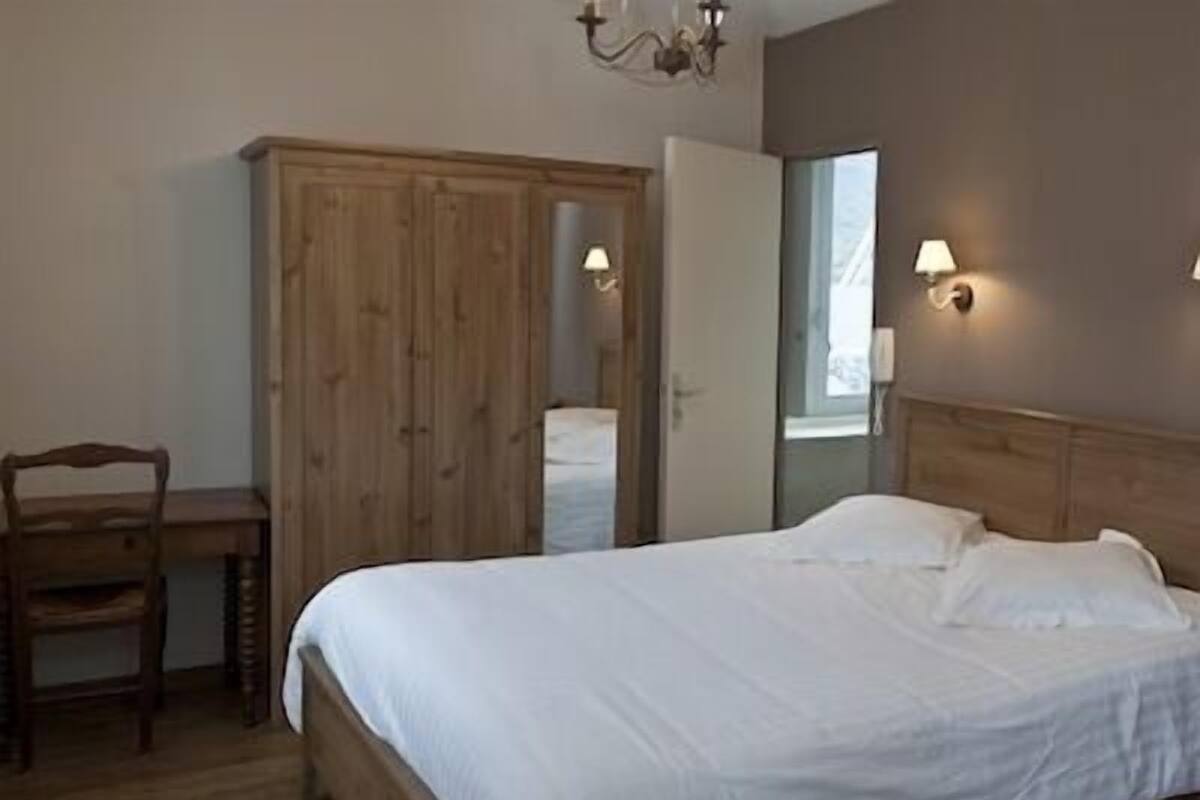 A bedroom with a wooden wardrobe, a bedside table, and a bed with white linens.