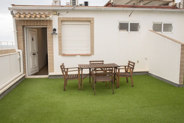 A patio with a wooden table and chairs, a door, and a window with shutters.