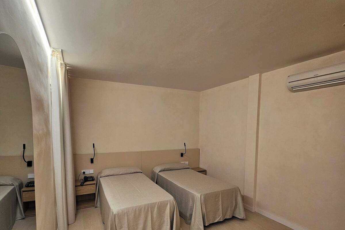 Ein Zimmer mit zwei Einzelbetten, Holzboden, Deckenventilator und Wand-Klimaanlage.