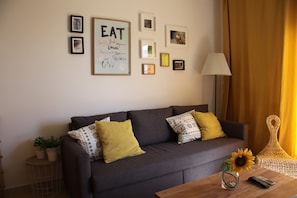 A living room with a grey sofa, yellow and patterned cushions, a small table with a vase of sunflowers, and a wall with framed pictures and a motivational quote. - Hotel El Globo (Valencia)