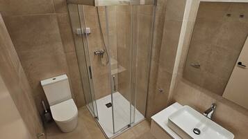 A modern bathroom with a glass-enclosed shower, a toilet, and a sink.
