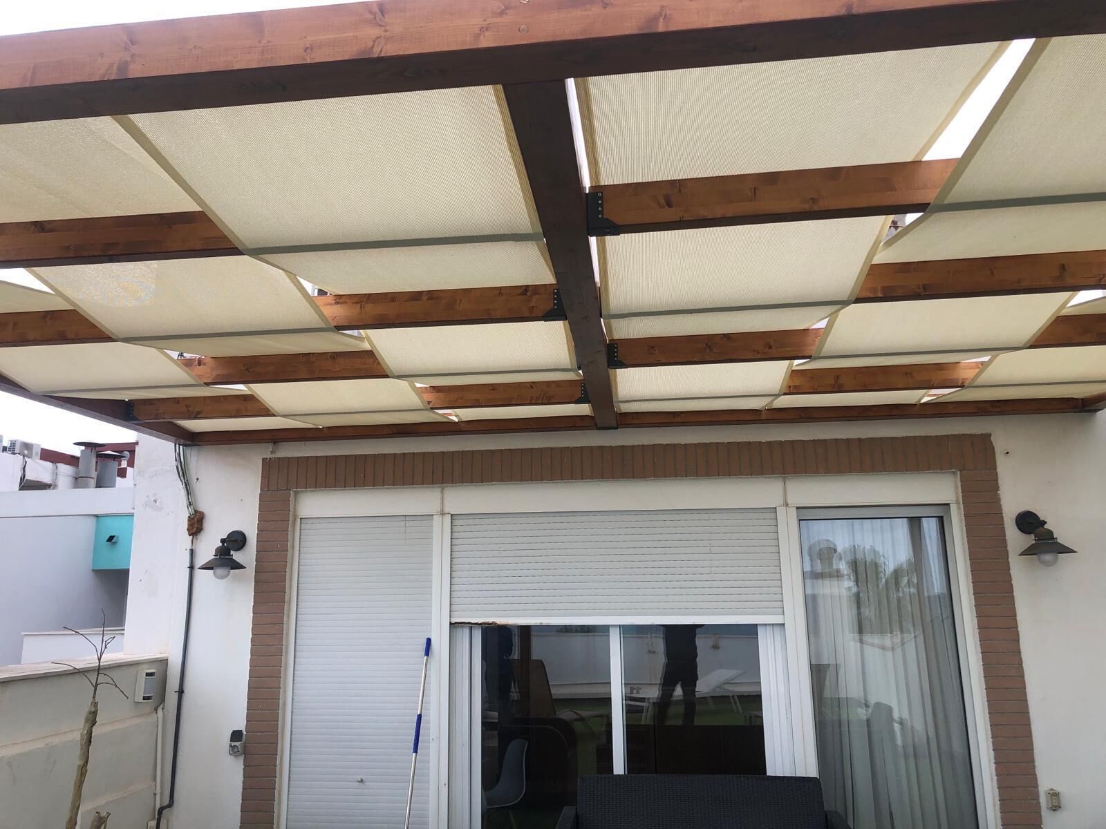 Un patio cubierto con puerta corredera de vidrio, vigas de madera y estructura de techo metálico.