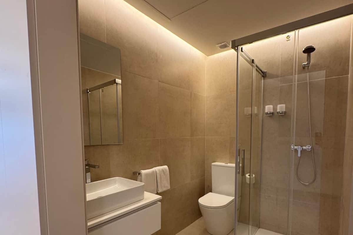 Ein modernes Badezimmer mit einer gläsernen Duschkabine, einem weißen Waschbecken und einer Toilette.