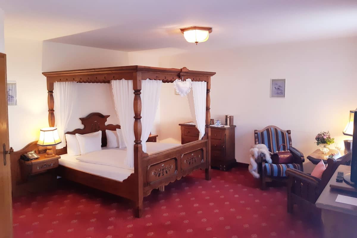 Een klassiek hemelbed, een nachtkastje met een lamp, een houten nachttafeltje, een stoel en een kleine tafel met een lamp en bloemen.