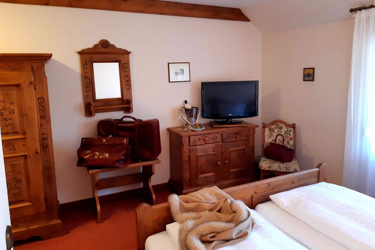 Een hotelkamer met een houten bed, een televisie op een houten dressoir, een spiegel, een houten kledingkast en een houten bureau met een rode tas en een glas.
