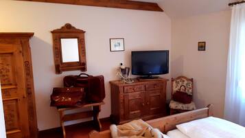 Ein Hotelzimmer mit einem hölzernen Bett, einem Fernseher auf einer Holzkommode, einem Spiegel, einem Holzschrank und einem Holztisch mit einer roten Tasche und einem Glas.