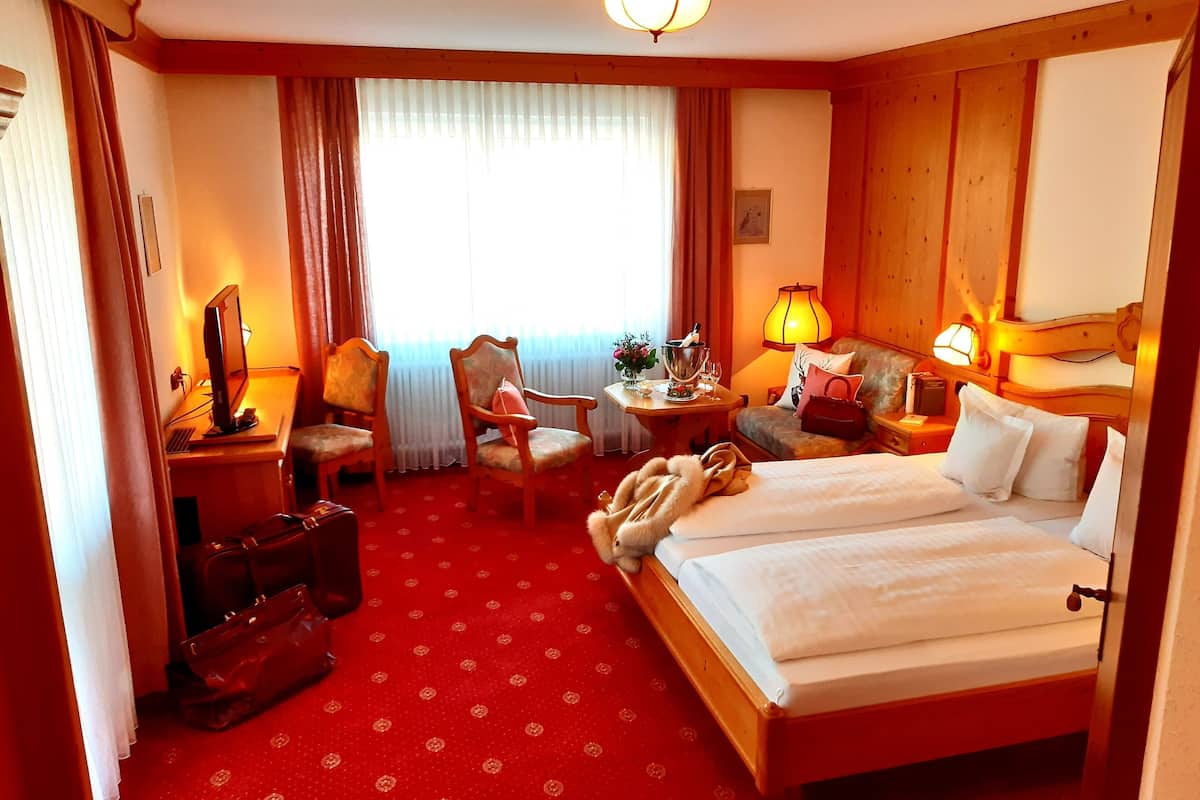 Een hotelkamer met een bed, twee stoelen, een bureau met een computer, een lamp en een raam met gordijnen.