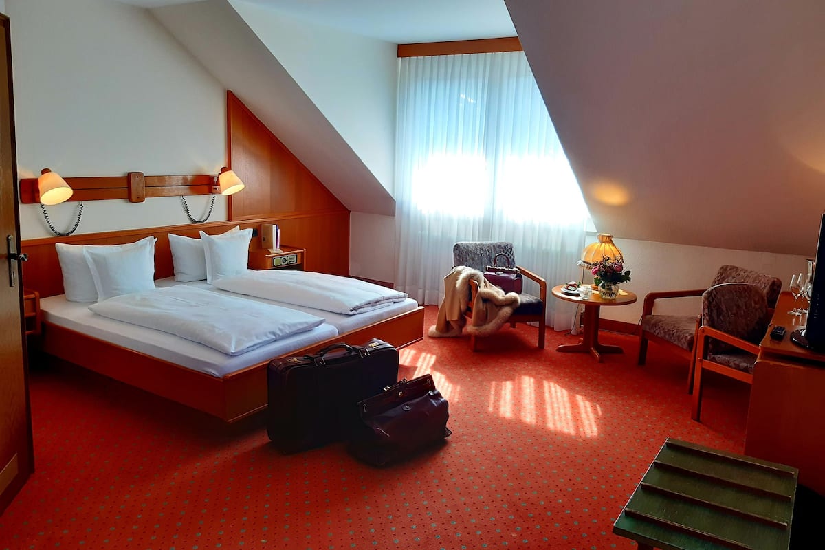 Een hotelkamer met een groot bed, een bureau met een lamp, een stoel en een tafeltje met een bloemenvaas.