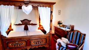 A four-poster bed with a canopy, a wooden dresser, a striped armchair, and a small table with a vase of flowers.