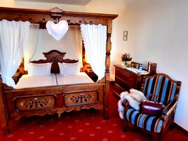 Una cama con dosel, un aparador de madera, un sillón a rayas y una mesita con un florero.