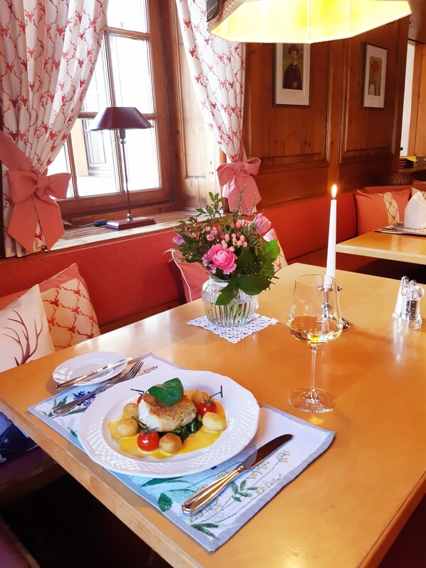 A dining table with a candle, a vase of flowers, and a plate of food. - Gasthaus Auerhahn (Baden-Baden)