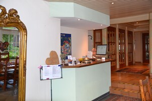 Una zona de recepción con un mostrador de madera, un espejo grande, un cartel llamativo y un monitor de ordenador.