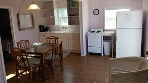 A kitchen with white cabinets, a dining table with chairs, a stove, a refrigerator, and a clock on the wall.
