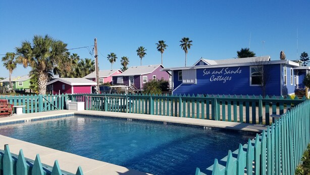 A pool area with a blue building labeled "Sea and Sands Cottages" and a green fence.