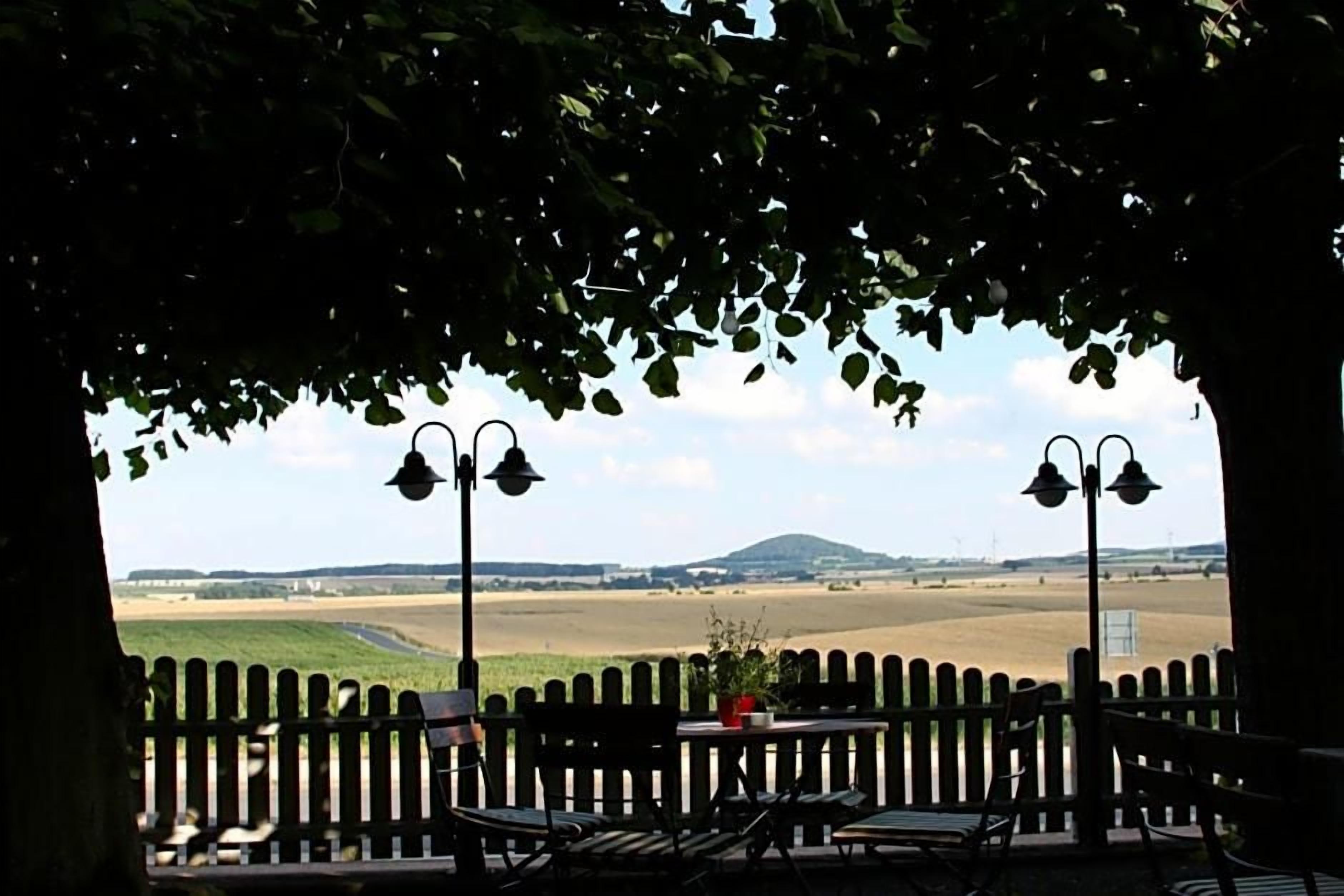 Une vue depuis un balcon doté d’une balustrade en bois, de deux chaises et d’une table sur laquelle est posée une plante en pot.