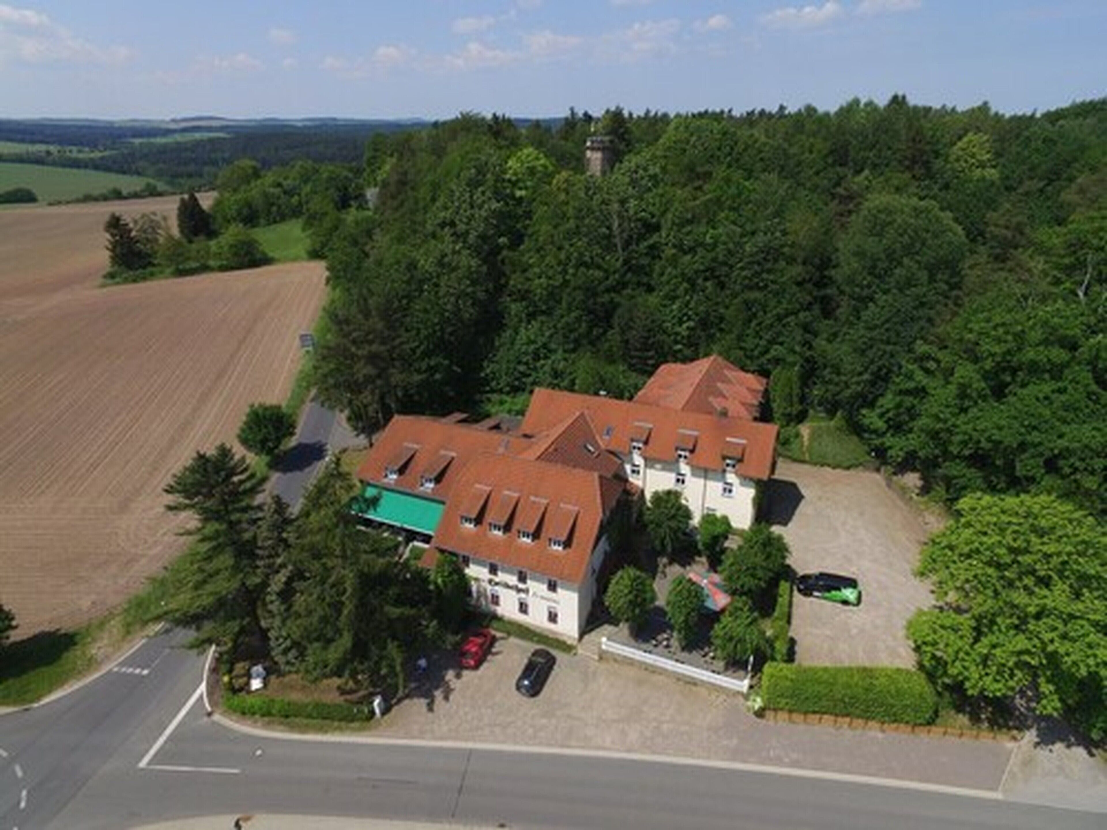 Ein großes, zweistöckiges Gebäude mit rotem Dach, umgeben von üppiger Vegetation und einem Feld.