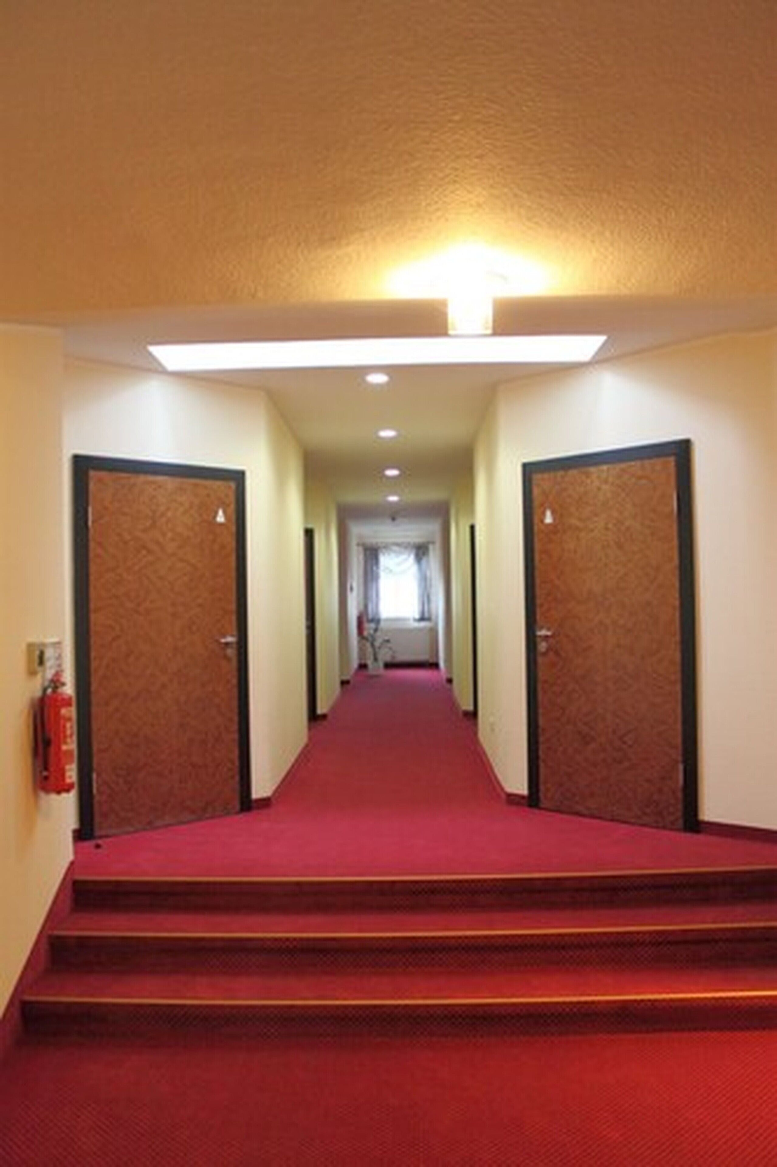 A hotel hallway with carpeted stairs, doors on either side, and a light fixture above.