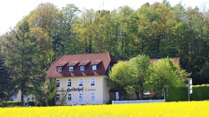 Un hotel con techo de tejas rojas, rodeado por un campo de flores amarillas y árboles frondosos.