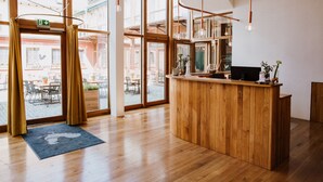 A wooden reception desk in a bright room with large windows, a blue rug, and hanging pendant lights. - Hotel Gut Hühnerhof (Gruendau)