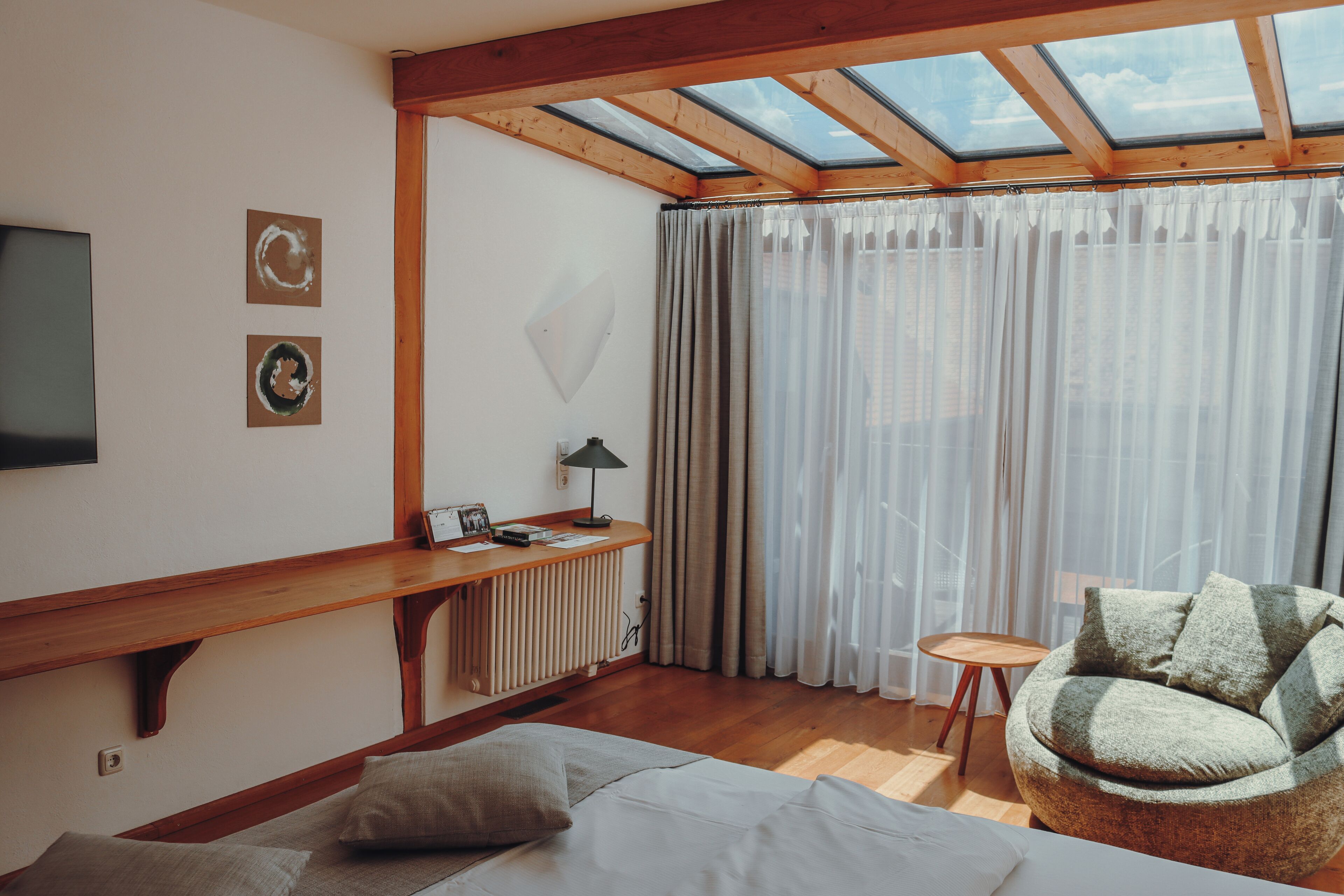 Een kamer met een bed, een stoel, een bureau met een lamp, een televisie en een raam met gordijnen.