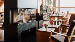 A wooden interior with a fireplace, wooden furniture, and large windows. - Hotel Gut Hühnerhof (Gruendau)