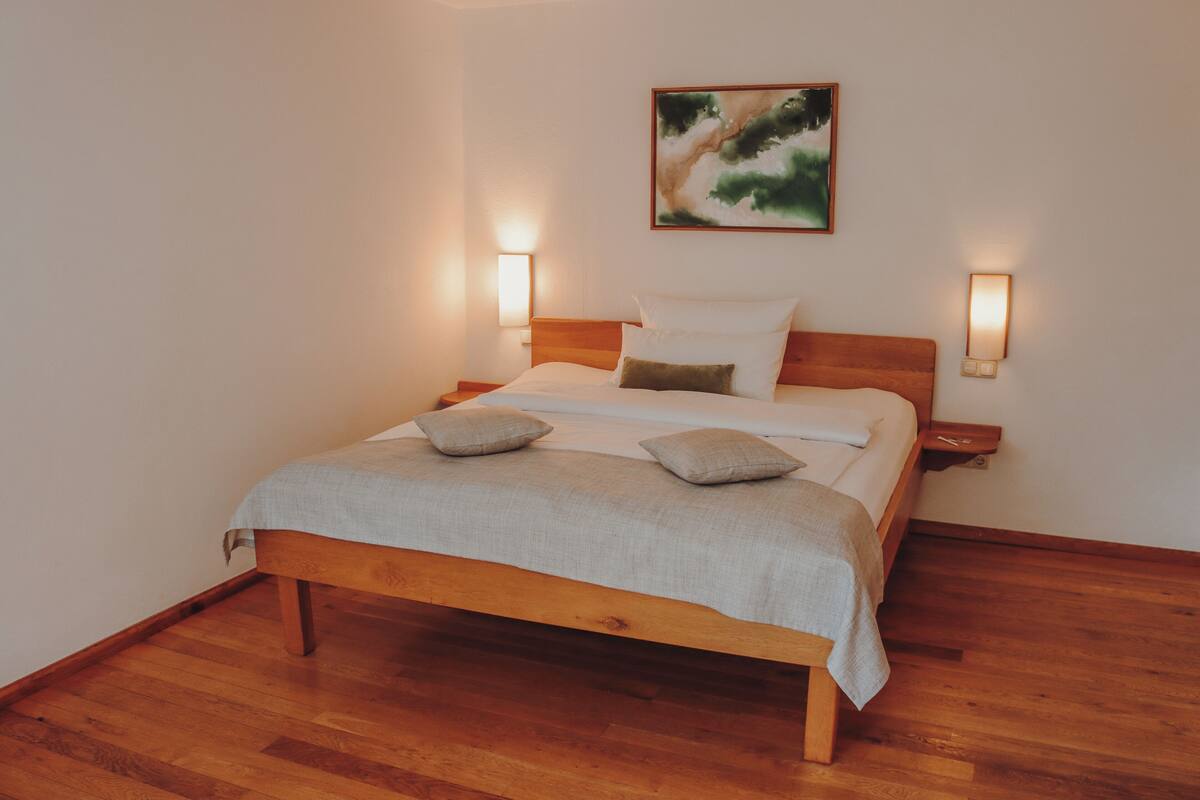 Een slaapkamer met een houten bed, twee bedlampen, een schilderij aan de muur en een houten vloer.