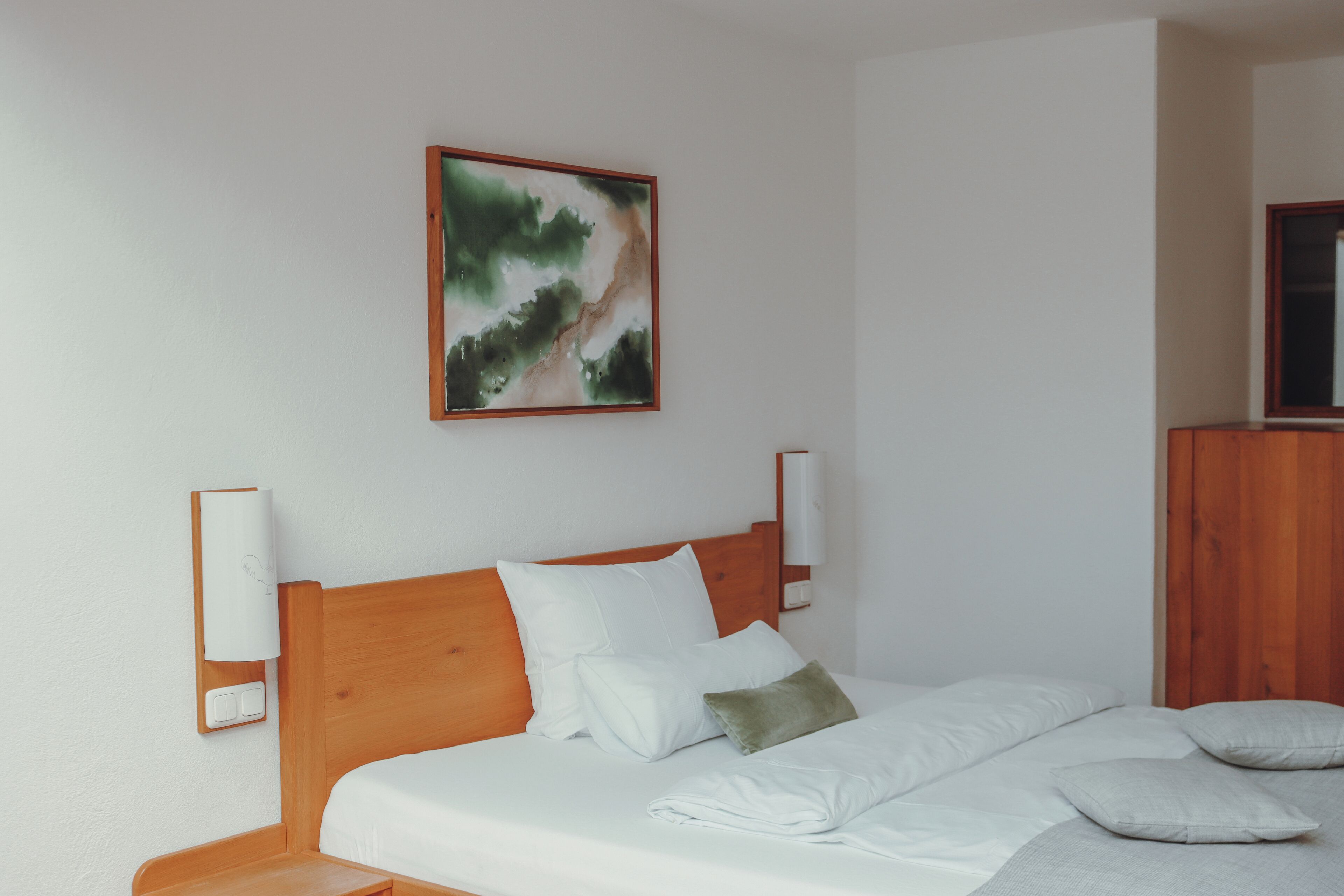 Ein ordentlich bezogenes Bett mit weißen Leinen und Kissen, ein hölzerner Kopfteil und ein an der Wand hängendes Gemälde.