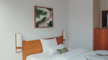 Ein ordentlich bezogenes Bett mit weißen Leinen und Kissen, ein hölzerner Kopfteil und ein an der Wand hängendes Gemälde.