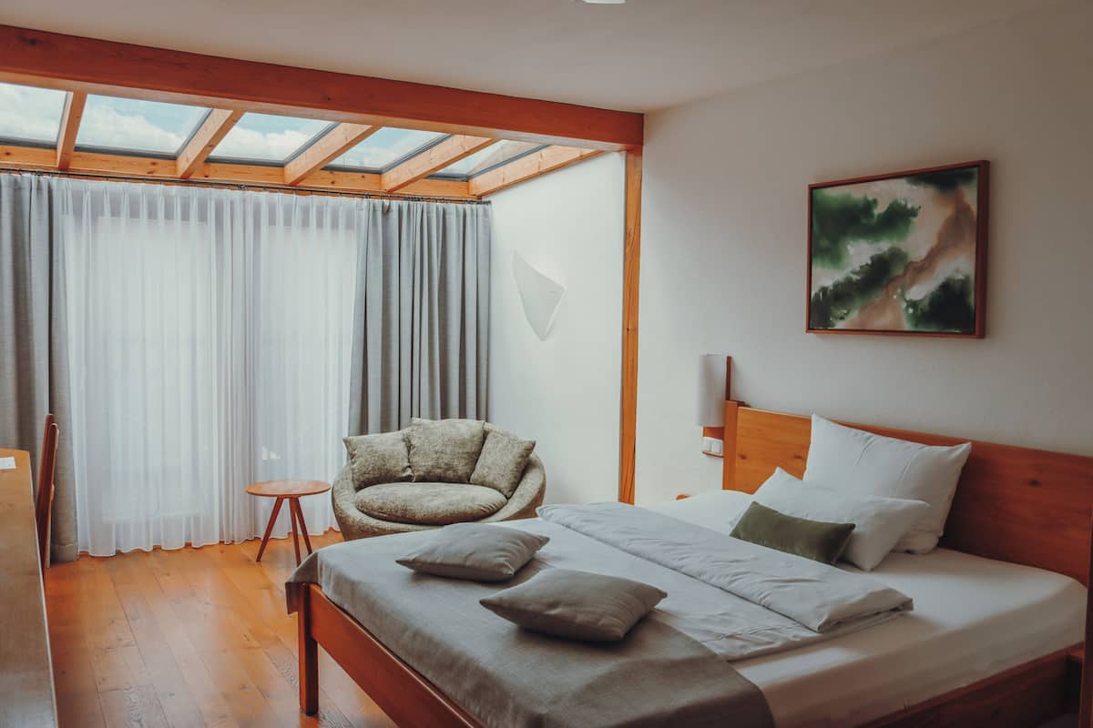 Een slaapkamer met een bed, een stoel, een klein tafeltje, een schilderij en een dakraam.
