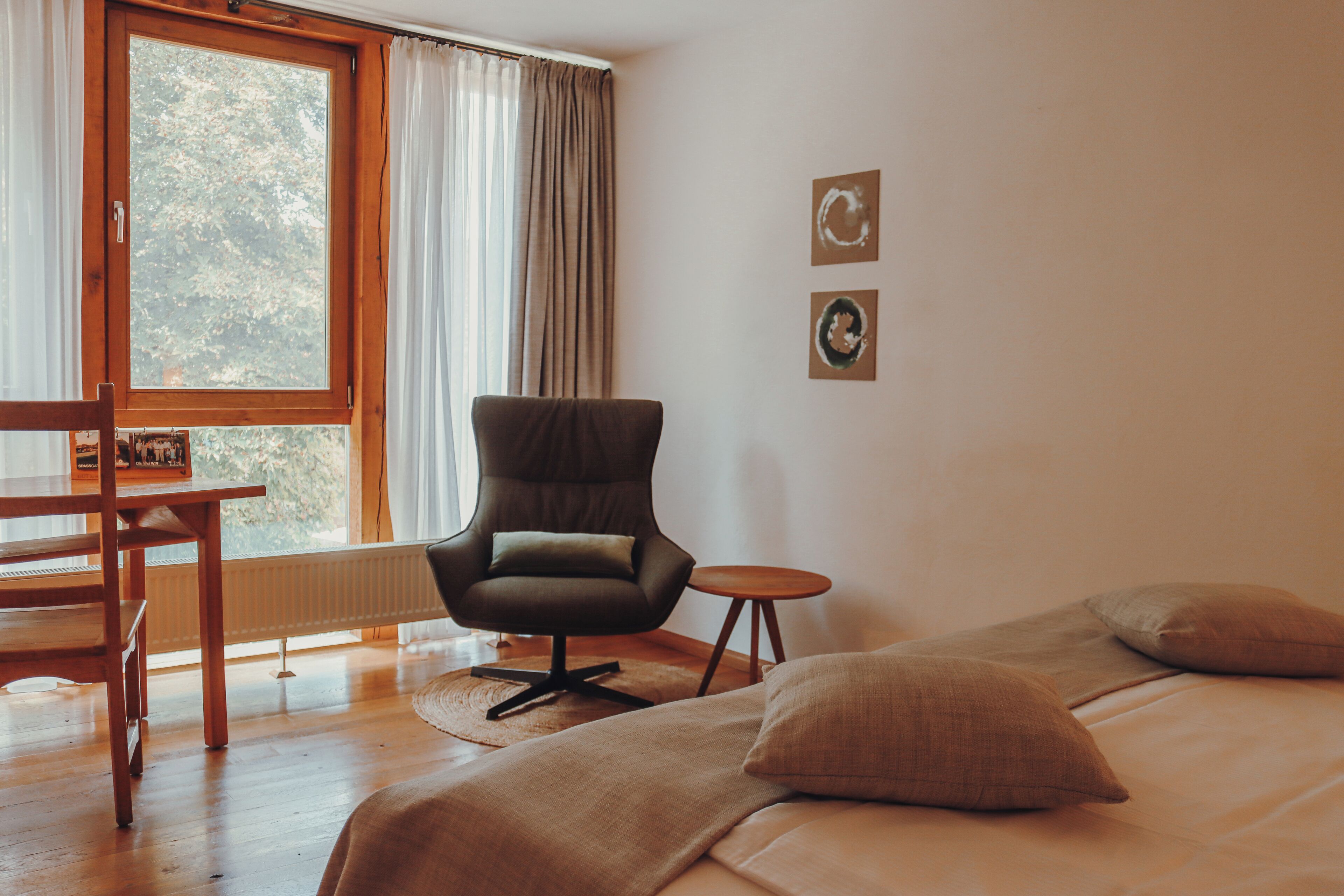 Une pièce comprenant un lit, une chaise, une petite table et une fenêtre avec des rideaux.