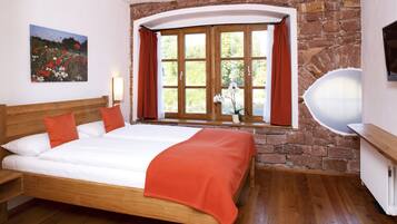 A bedroom with a wooden bed, a stone wall, a window with curtains, and a painting on the wall.