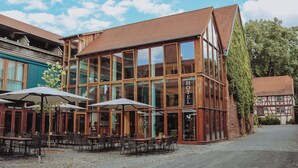 A hotel with a traditional facade, large windows, and outdoor seating with umbrellas. - Hotel Gut Hühnerhof (Gruendau)