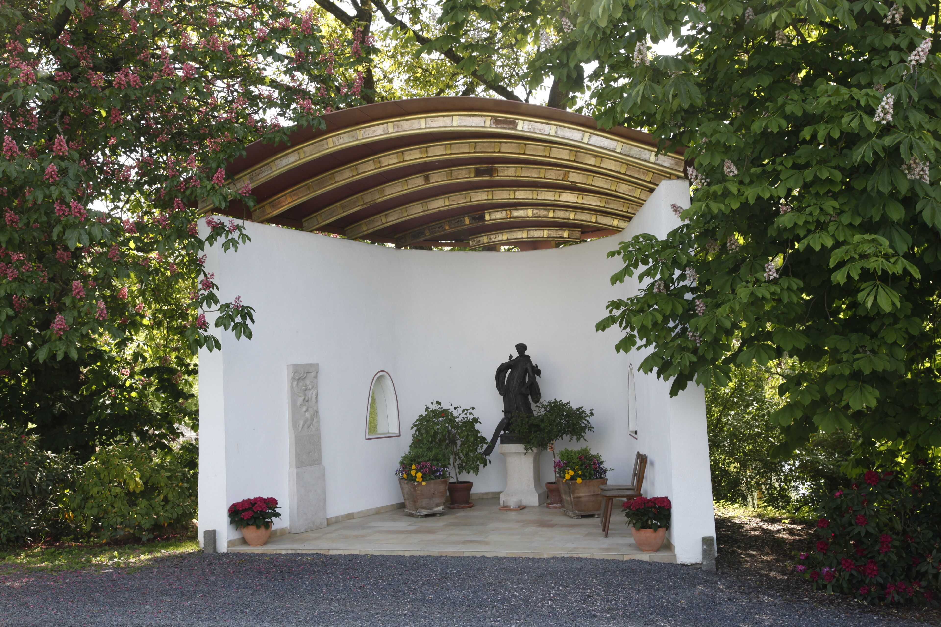 A garden with a white wall, a statue, and potted plants.