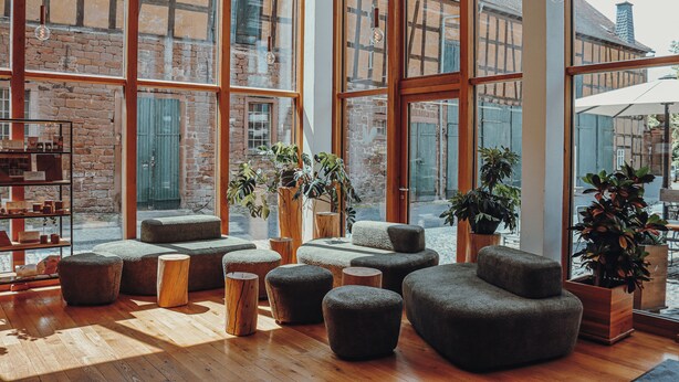 A modern interior with large windows, wooden flooring, and multiple seating areas. - Hotel Gut Hühnerhof (Gruendau)