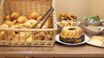 A variety of breads and pastries in a basket and on plates, with a wooden table and stacked plates underneath.