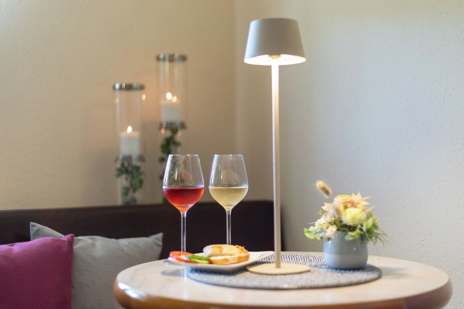 A table with two wine glasses, a small vase with flowers, and a candle holder in the background.