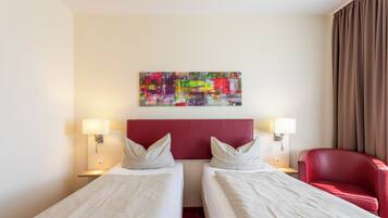 A hotel room with two beds, a red headboard, a colorful abstract painting, and a red armchair.